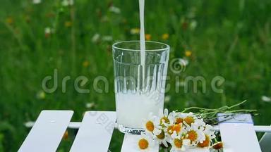 特写镜头。 放慢脚步。 将牛奶倒入玻璃烧杯中.. 旁边躺着一束雏菊。 在这种背景下